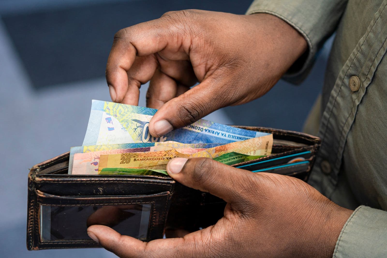 A man counts South African rand notes from his wallet, the kind of cash a SARS tax refund pays out.