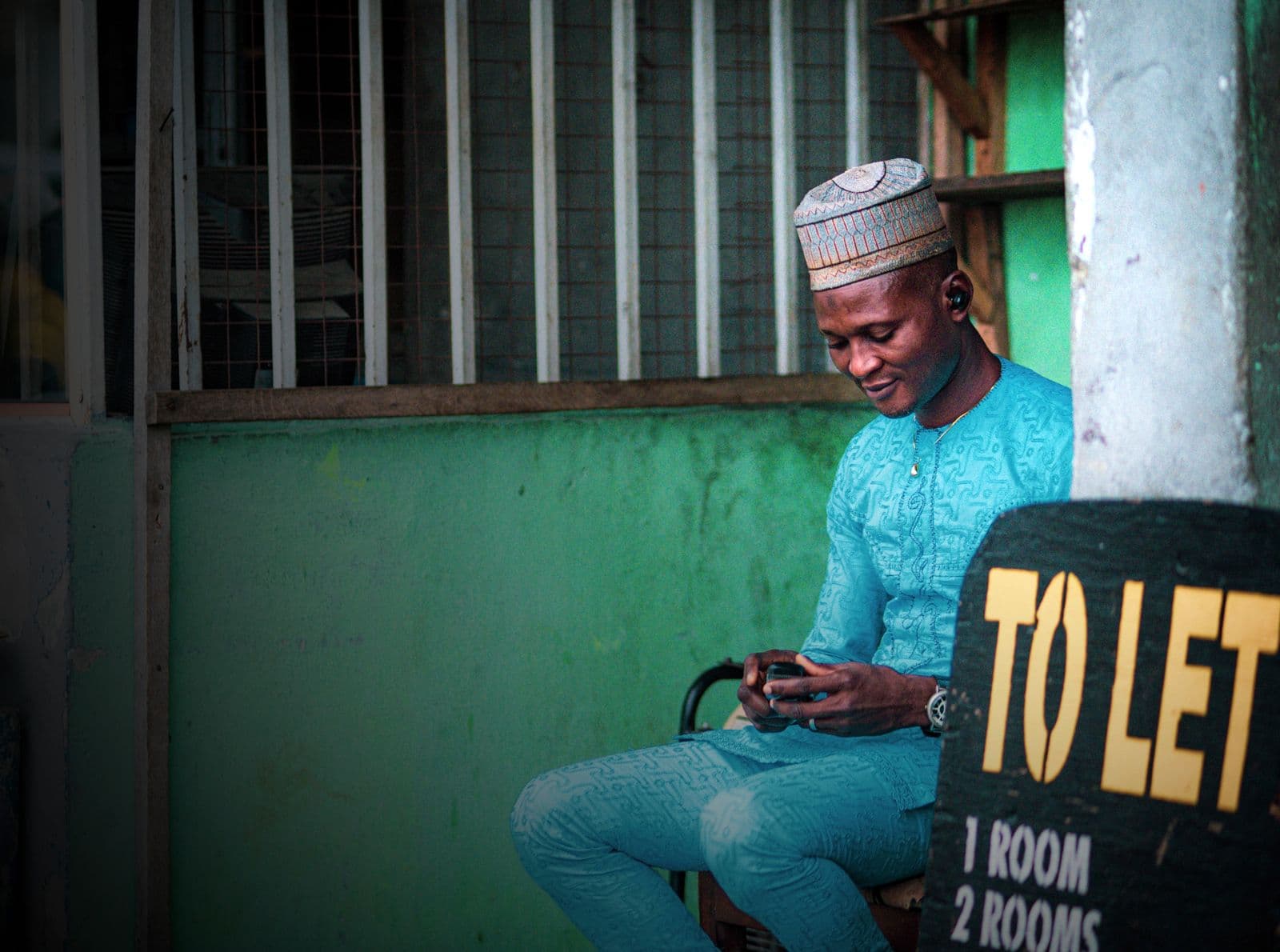 A Nigerian man checking his phone outdoors, the kind of USSD check used to look up a BVN