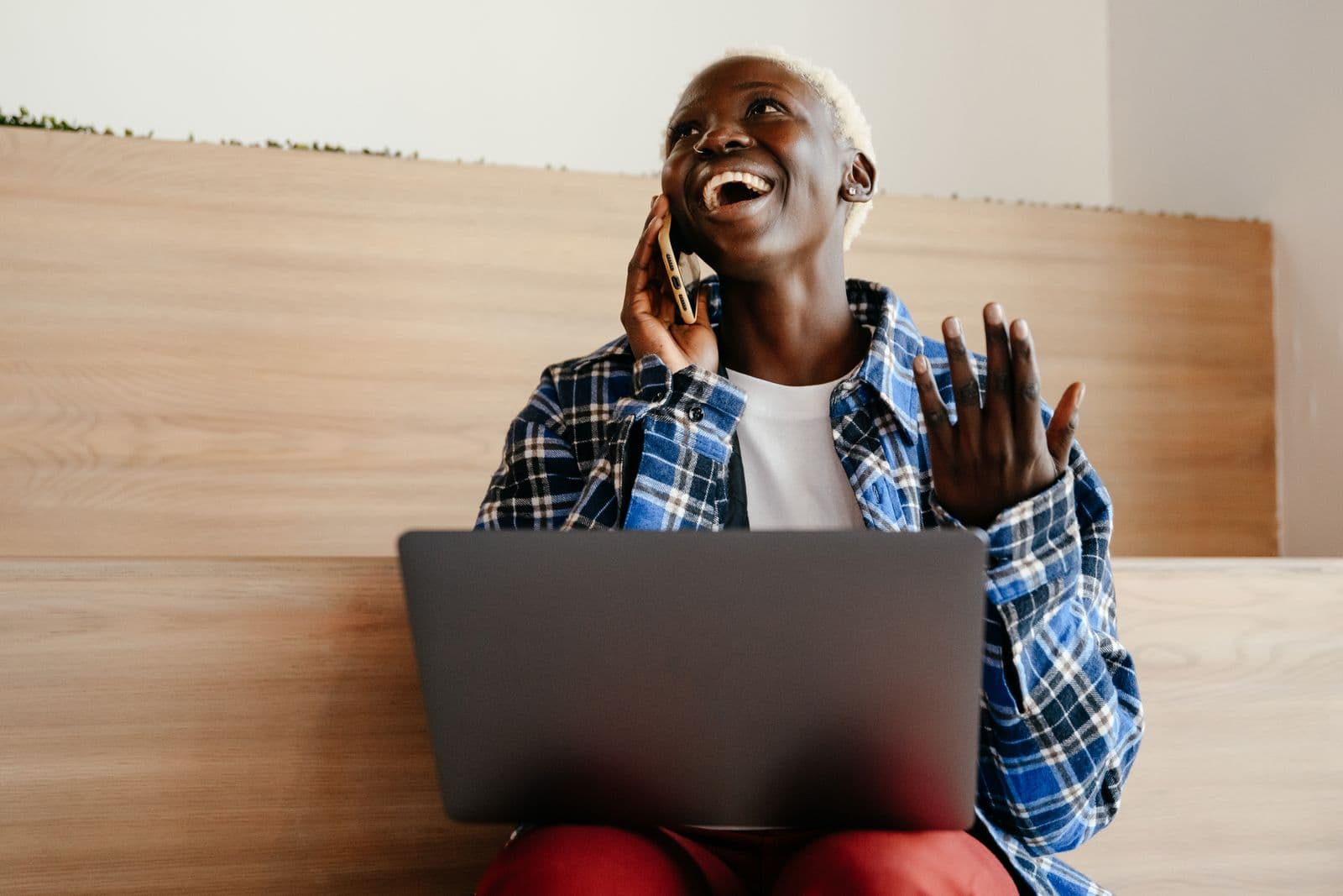 A smiling Kenyan freelancer checks a mobile money payment notification on her phone while working on her laptop.