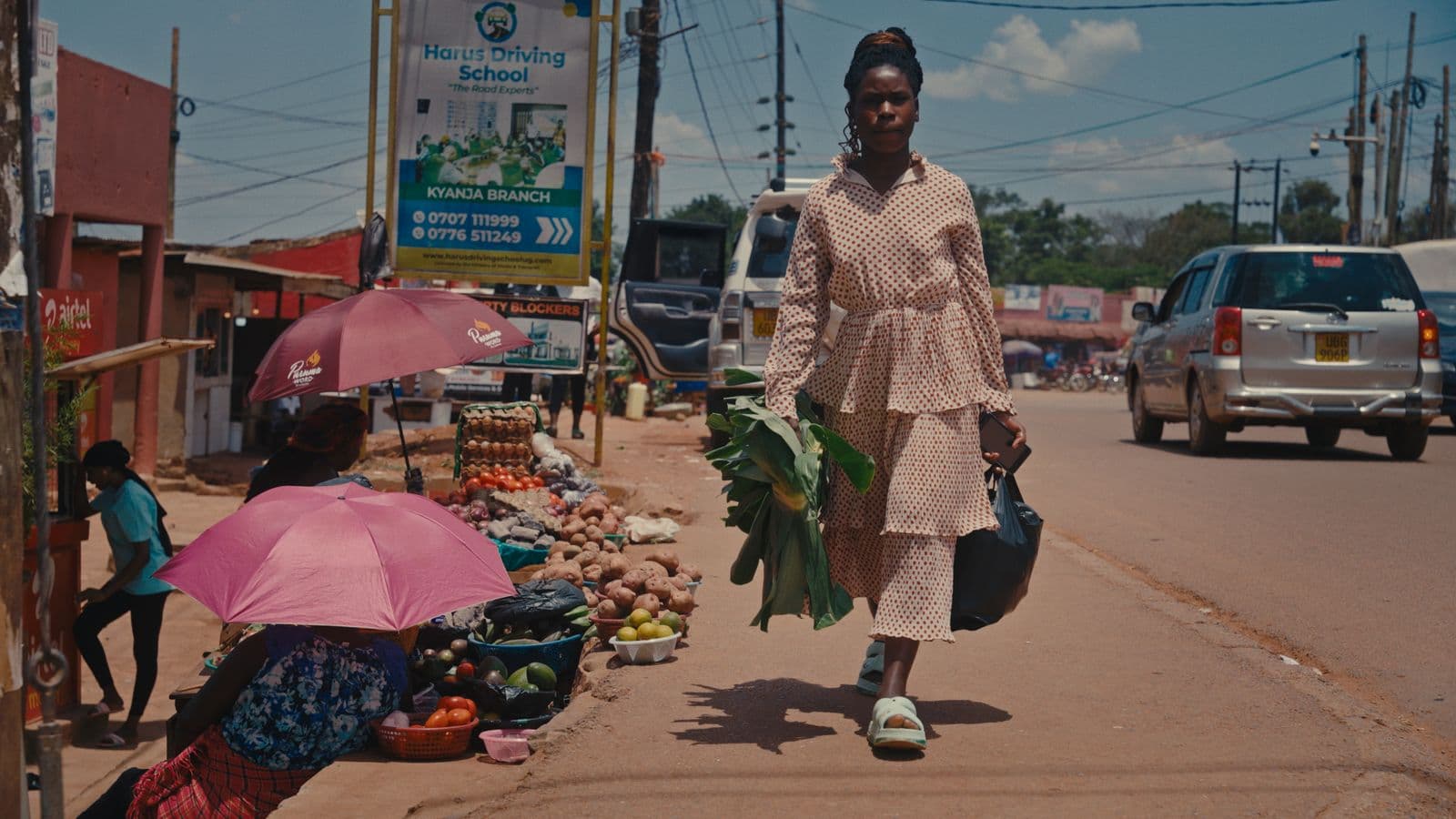 A woman walks past an outdoor fruit market stall on a street in Uganda