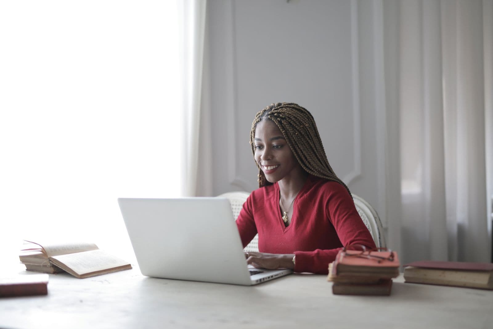 A woman with braided hair smiling while working on her laptop at home, the kind of remote work setup Africans use to earn in foreign currency.