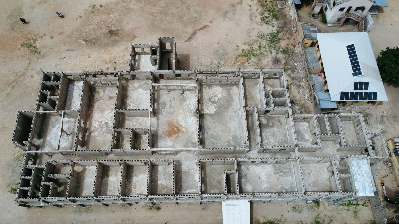 Aerial view of an unfinished concrete house under construction in Nigeria, showing the block walls and roof frame before finishing.