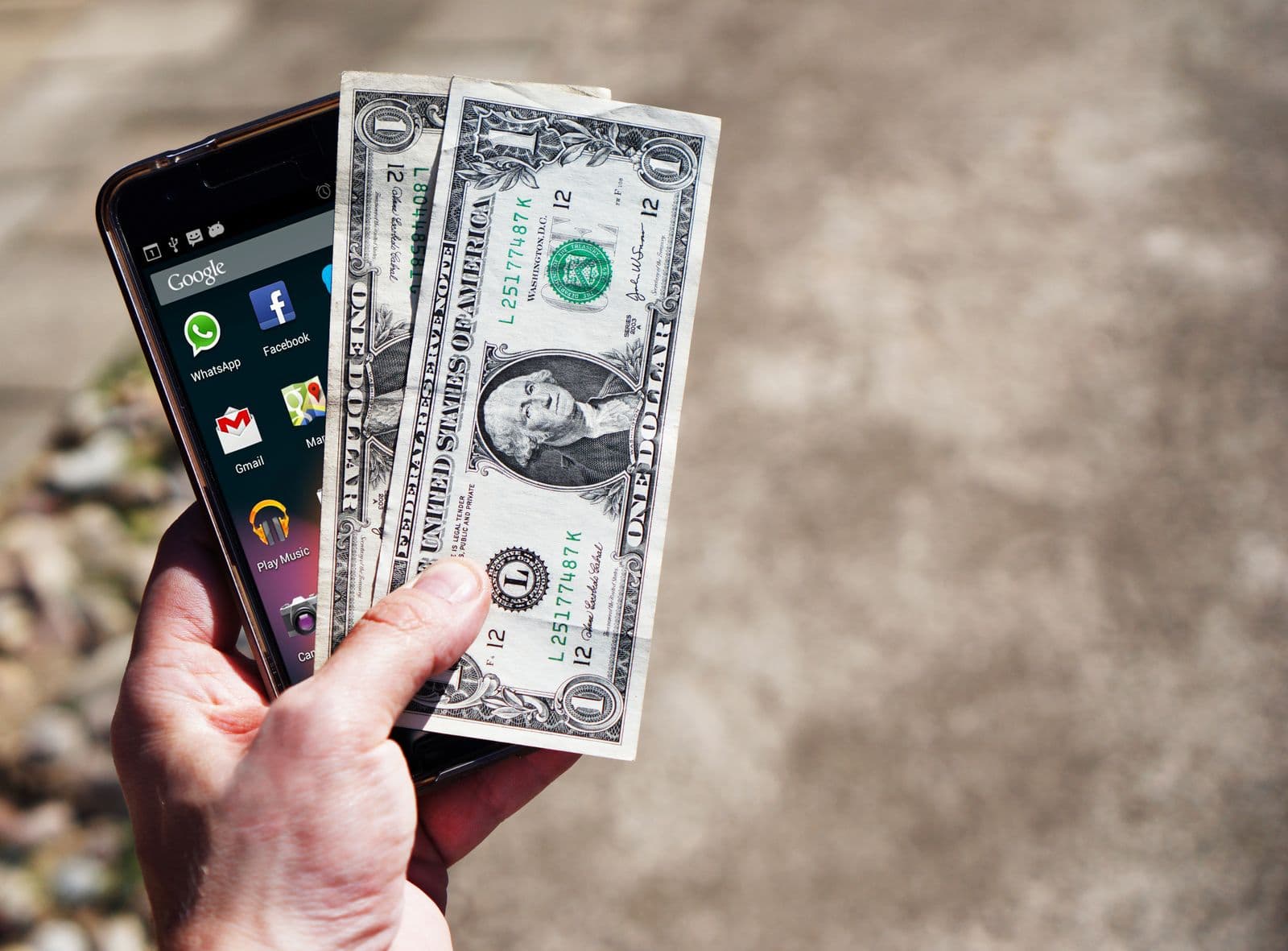 Hand holding US dollar notes and a smartphone, the kind of USD transfer EcoCash charges apply to