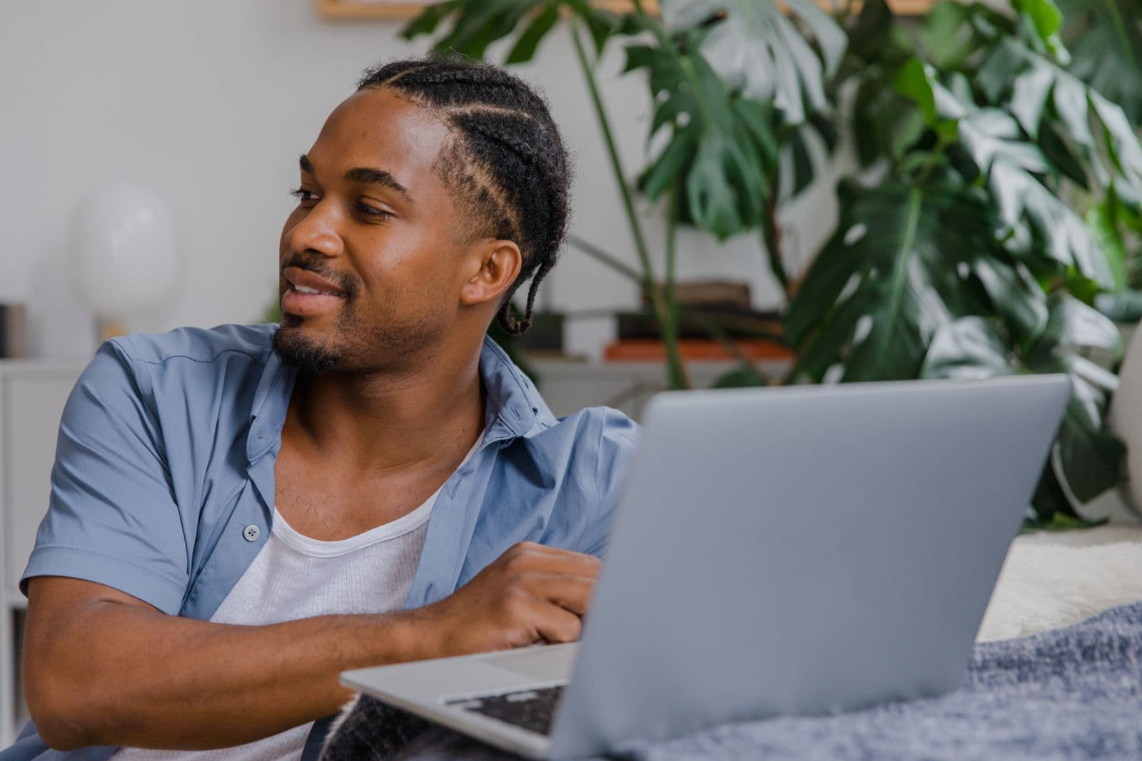 Young man with braided hair working on a laptop at home, the kind of remote AI training work Outlier offers